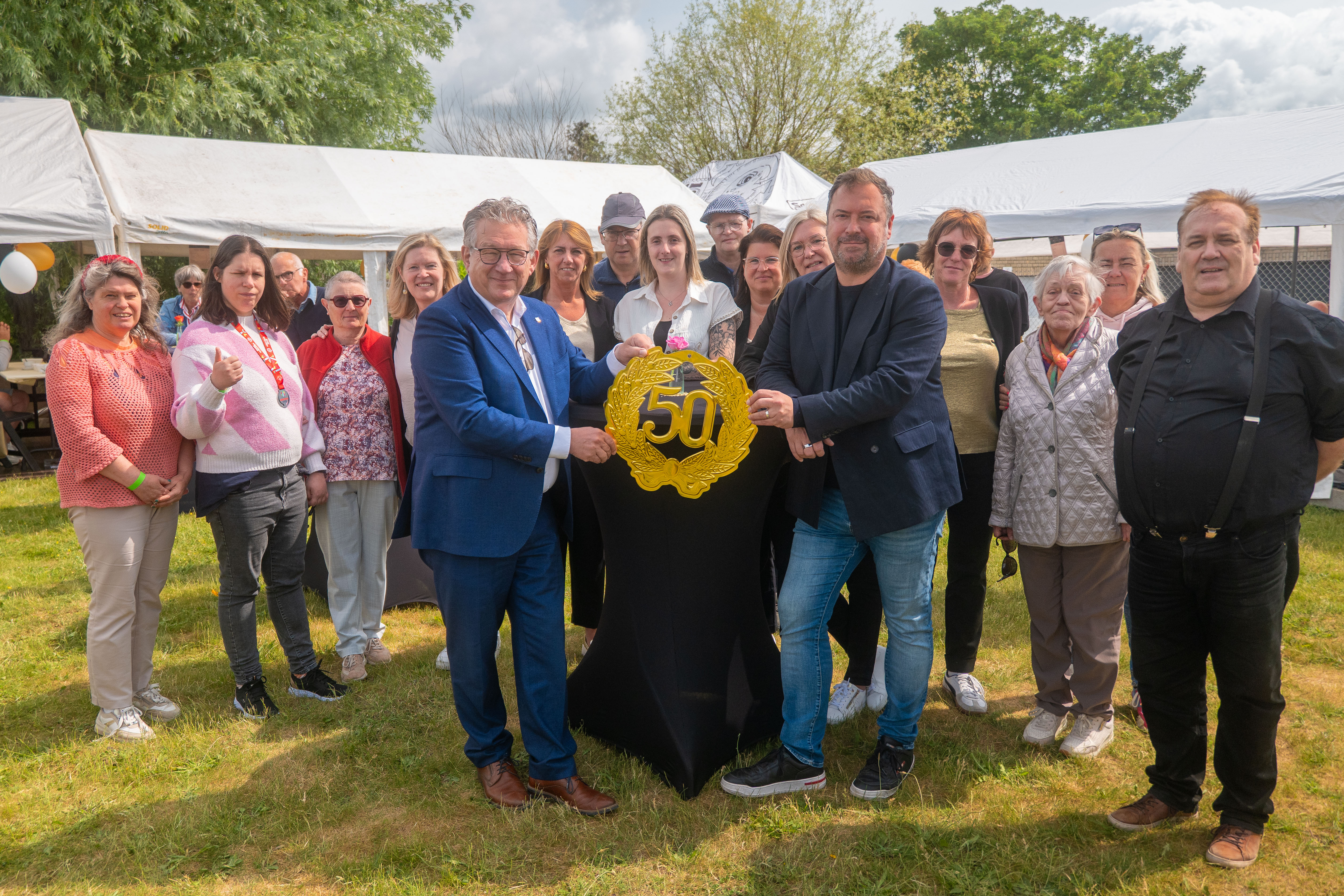 Burgemeester Dirk De fauw en schepen van sociale zaken Pablo Annys poseren met het '50 jaar jubileum-logo', omringt door de medewerkers van het buurtcentrum De Garve.